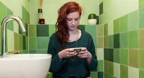 Foto de mujer enviando mensajes de texto mientras usa el baño