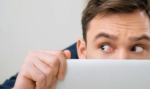 Zdjęcie mężczyzny chowającego się za laptopem