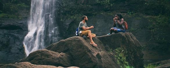 Schermata di due persone che parlano vicino a una cascata